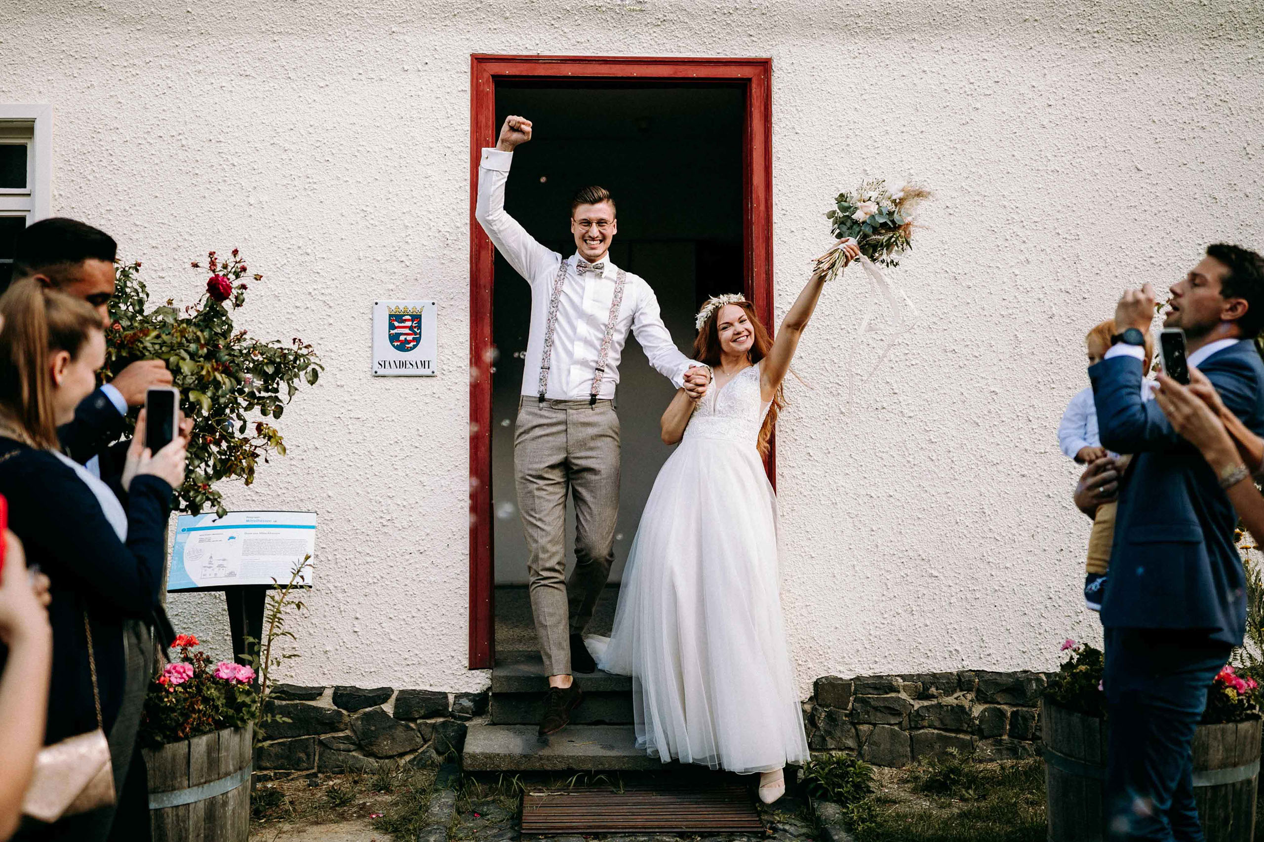 Hochzeitspaar verlässt jubelnd das Standesamt im Freilichtmuseum Hessenpark bei Bad Homburg – festgehalten vom Hochzeitsfotograf Bad Homburg.