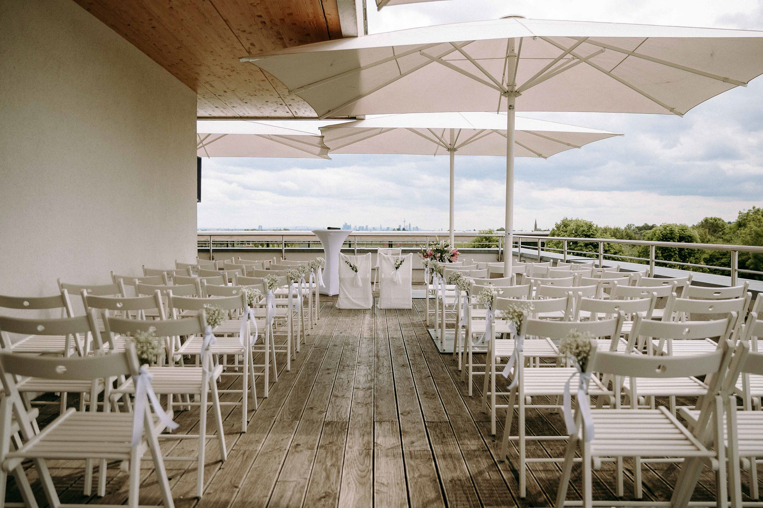 Stuhlreihen und dekorierter Trauplatz auf der Dachterrasse des Taktgefuehl Eventhaus mit Blick auf die Skyline