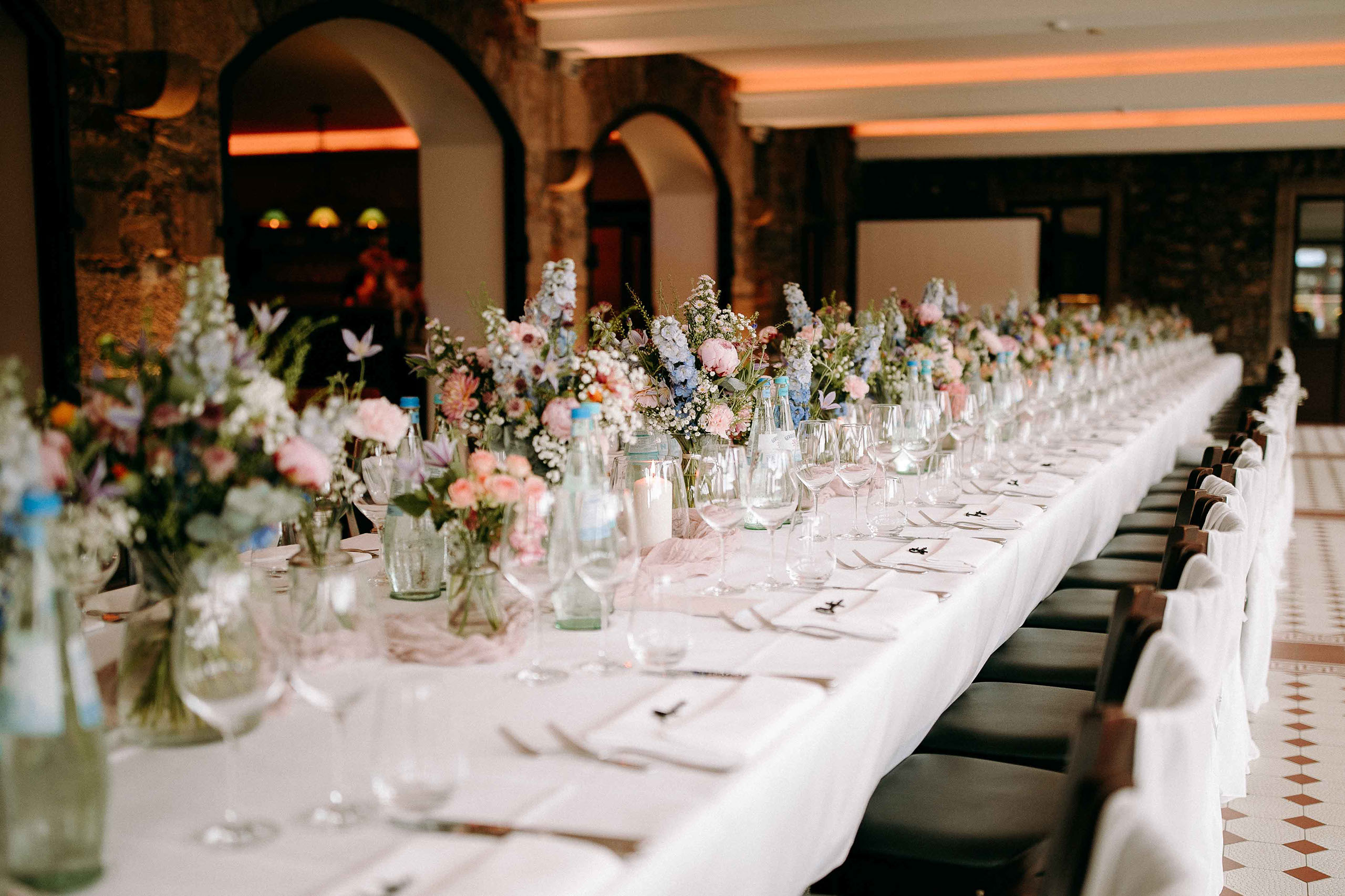 Lang gedeckte Hochzeitstische mit weißen Stuhlhussen und Blumenarrangements – Burg Reichenstein als traumhafte Hochzeitslocation.