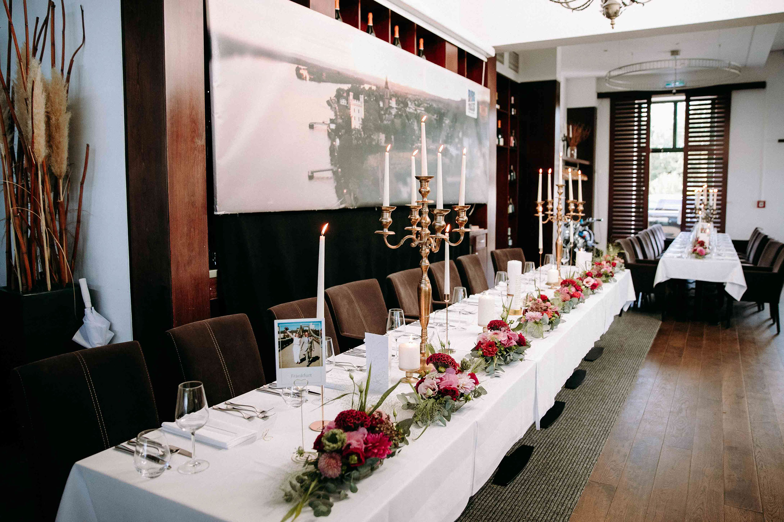 Lang gedeckter Hochzeitstisch mit Kerzen und Blumen im Festsaal von Burg Crass – Hochzeitslocation Rheingau.