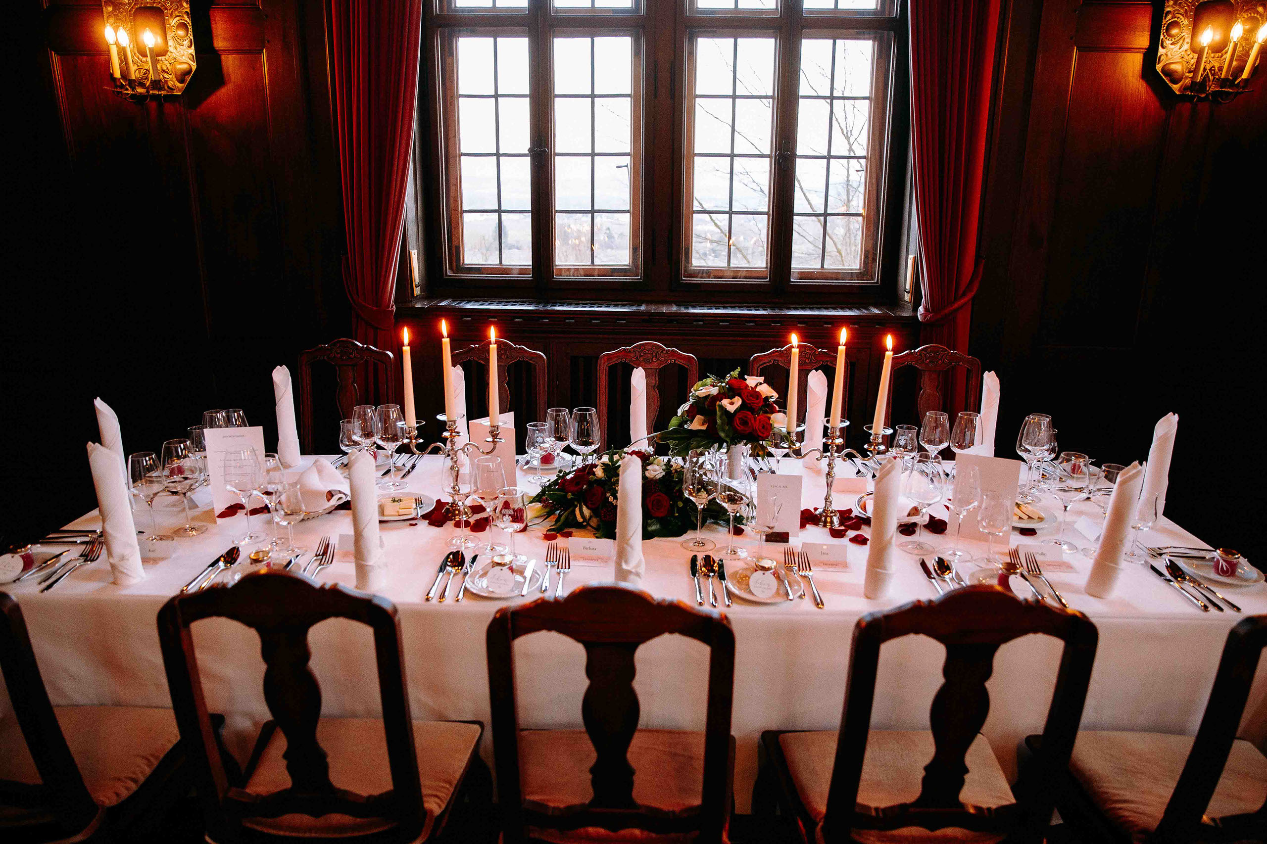 Romantisch gedeckter Tisch vor großen Fenstern im Schloss Vollrads mit Kerzen und floraler Dekoration