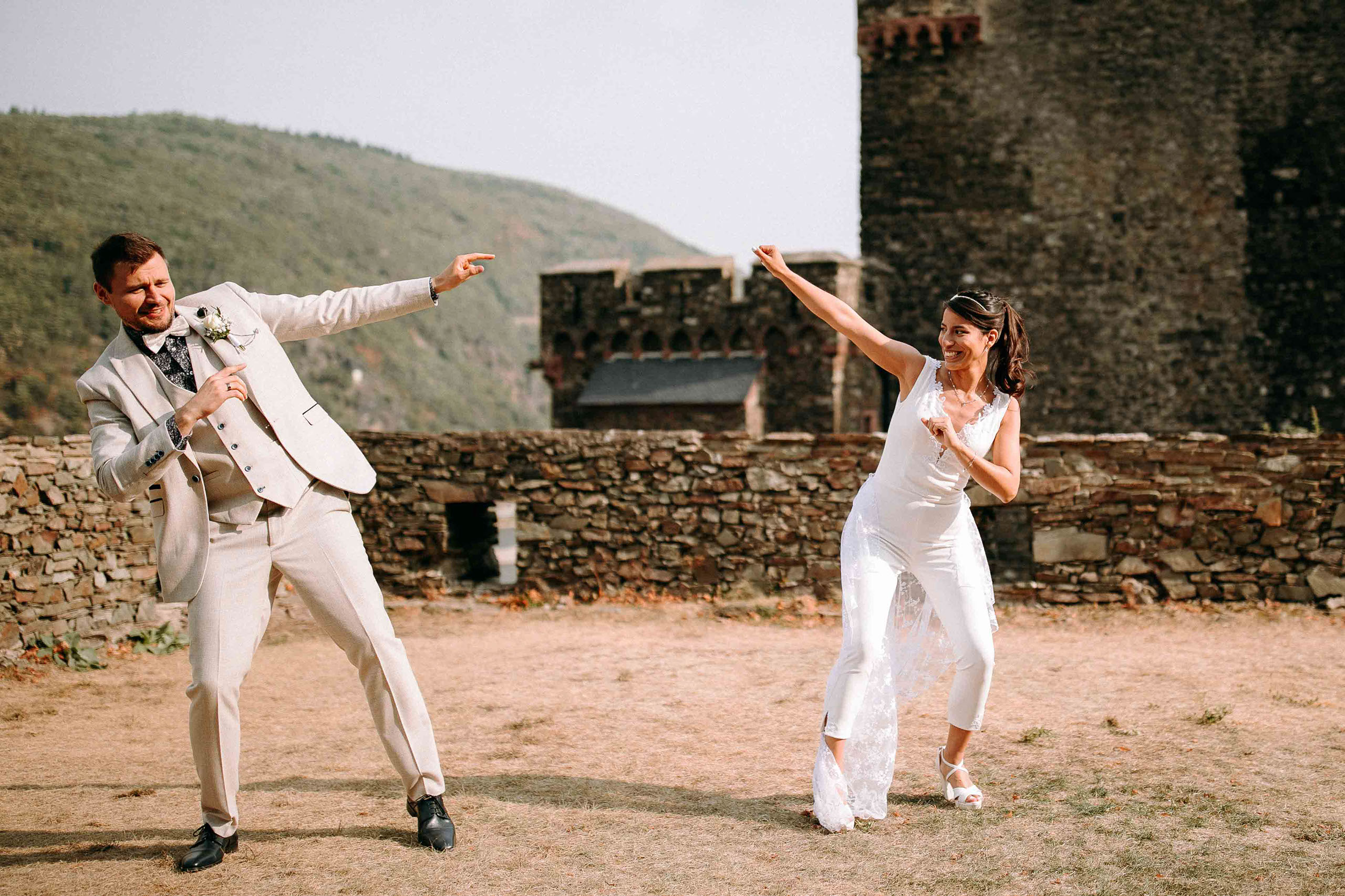 Fröhliches Brautpaar auf Burg Reichenstein posiert verspielt vor historischer Kulisse – Hochzeitsfotograf Rheingau