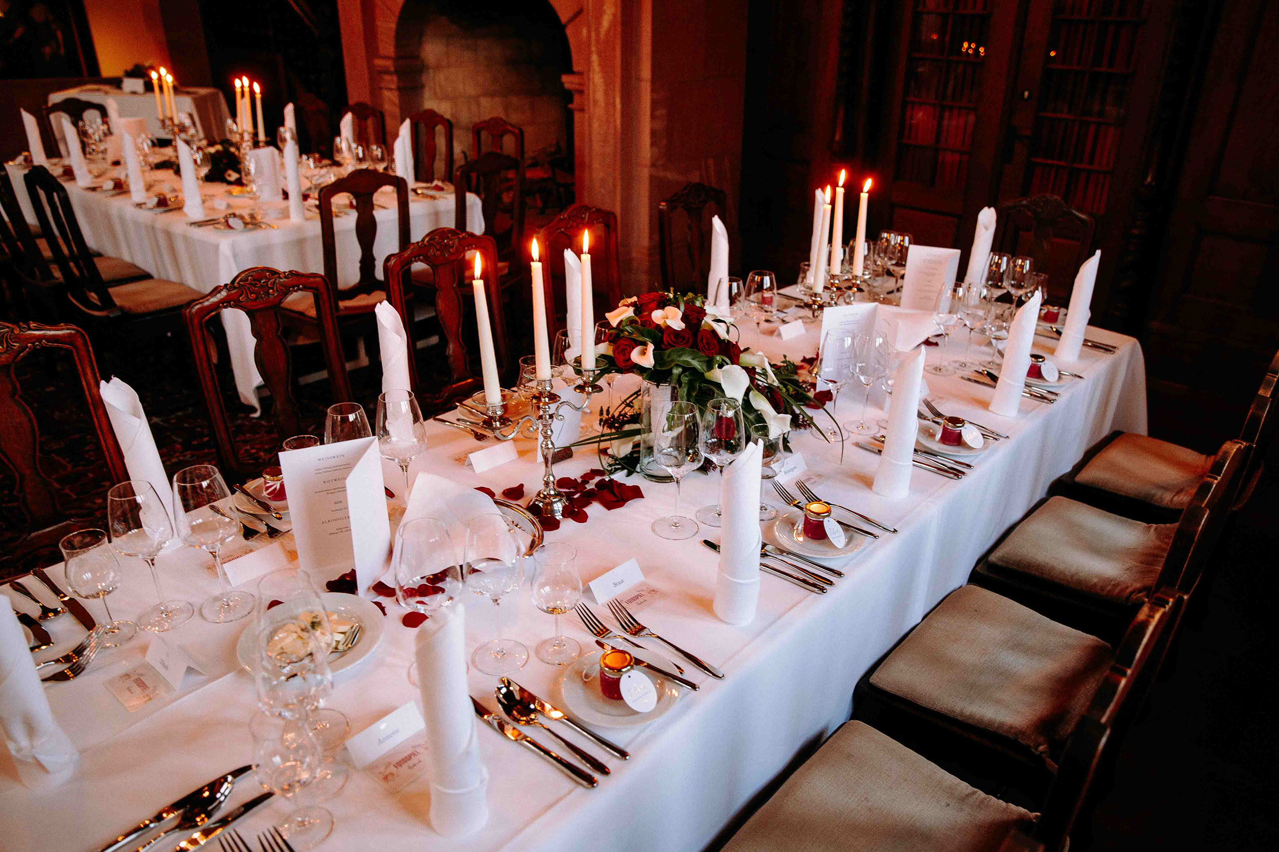 Elegante Hochzeitstafel mit weißen Servietten, Kerzen und Blumen in historischem Schlossambiente