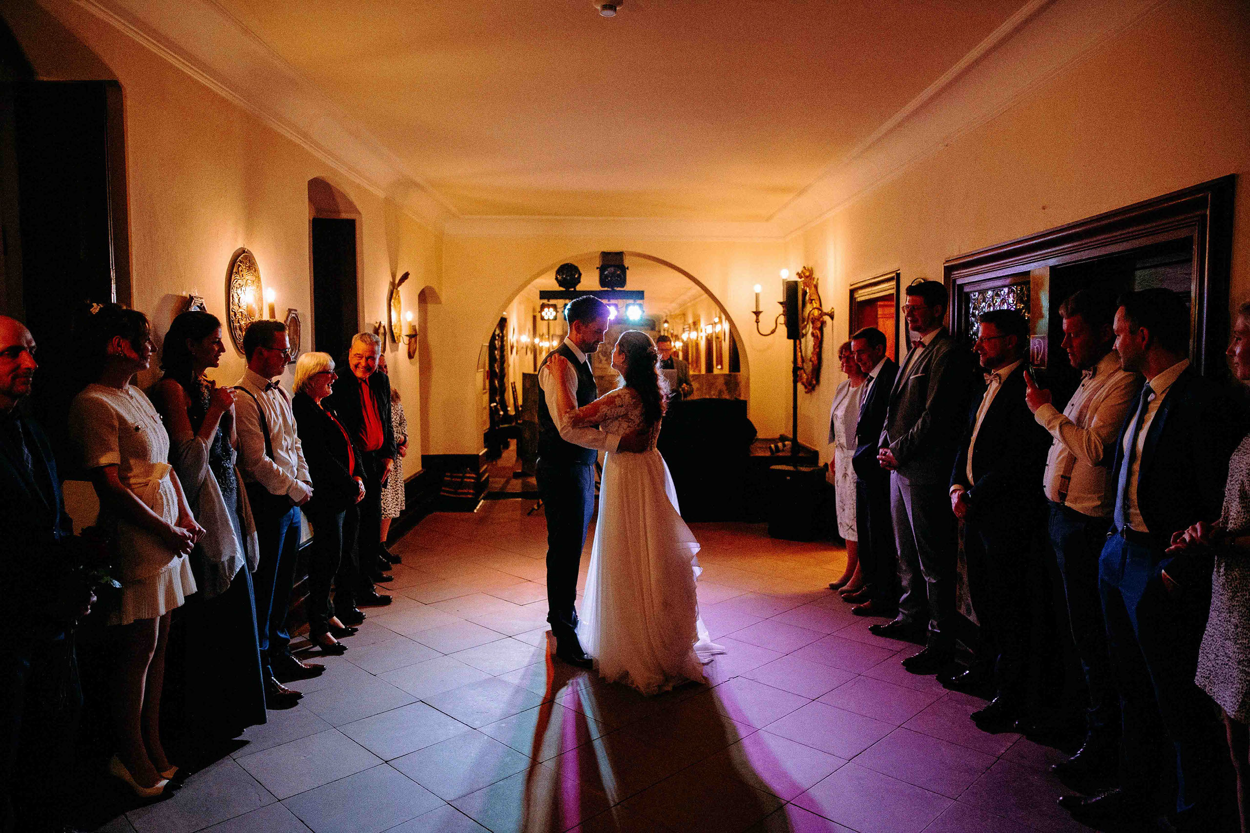 Brautpaar tanzt den Eröffnungstanz im beleuchteten Flur umgeben von Gästen