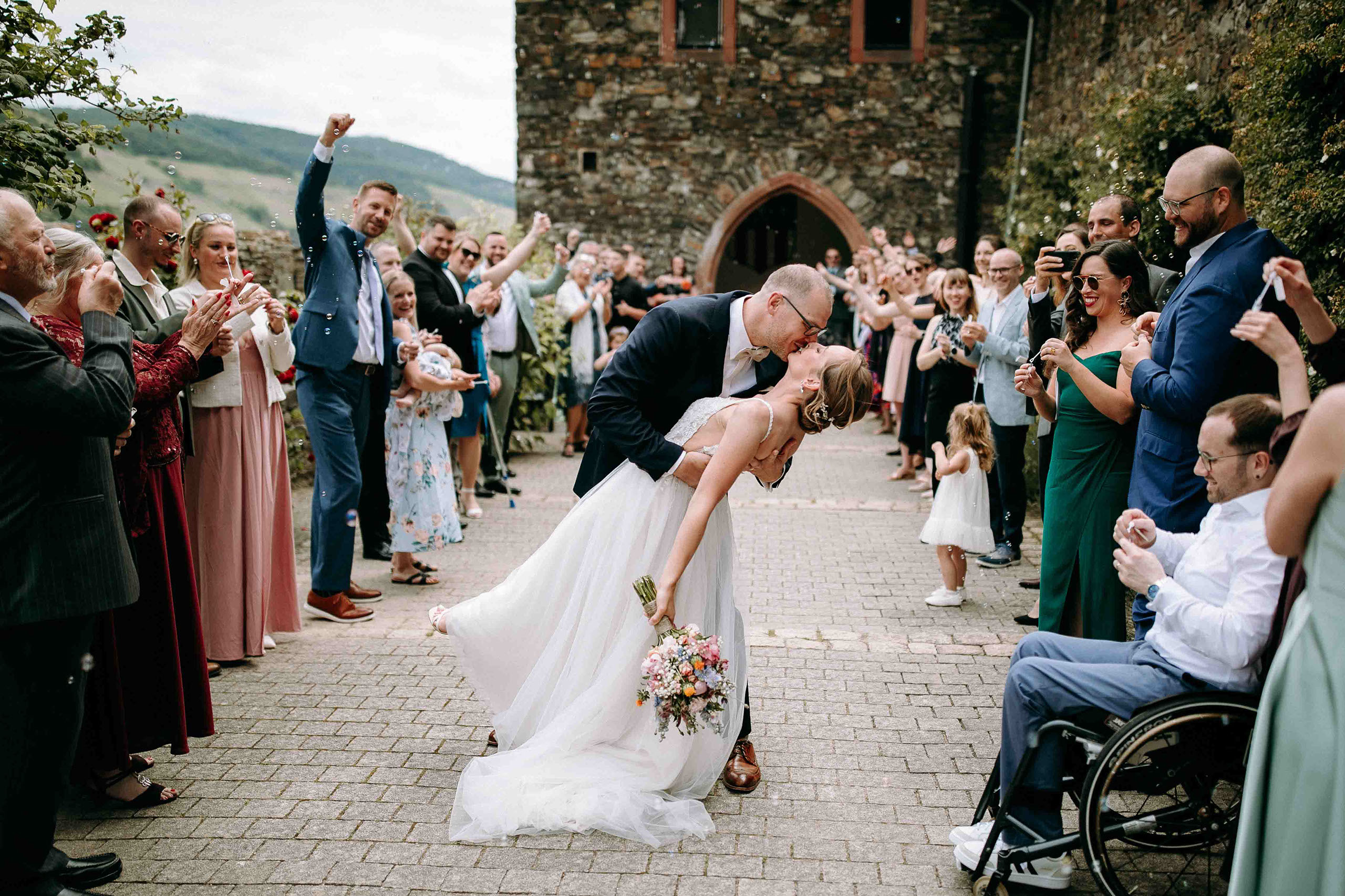Emotionaler Kuss des Brautpaars umgeben von applaudierenden Hochzeitsgästen – Hochzeitsfotograf Burg Reichenstein
