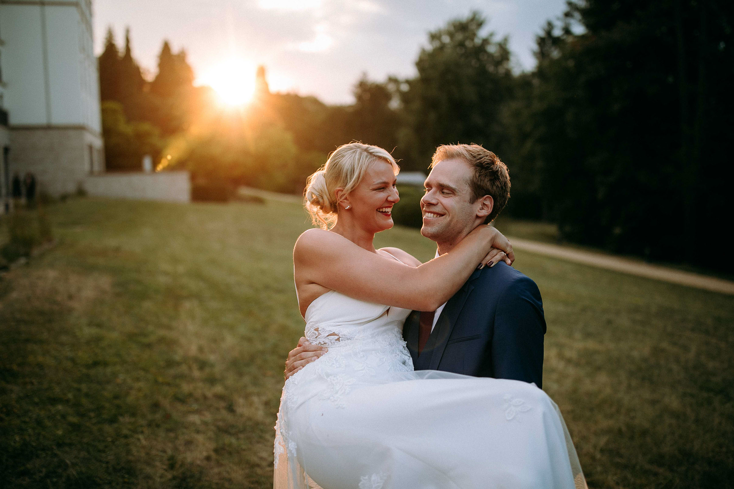 Lächelndes Brautpaar – der Bräutigam trägt die Braut im Sonnenuntergang – Hochzeitsfotograf Oberursel fängt den Moment ein.