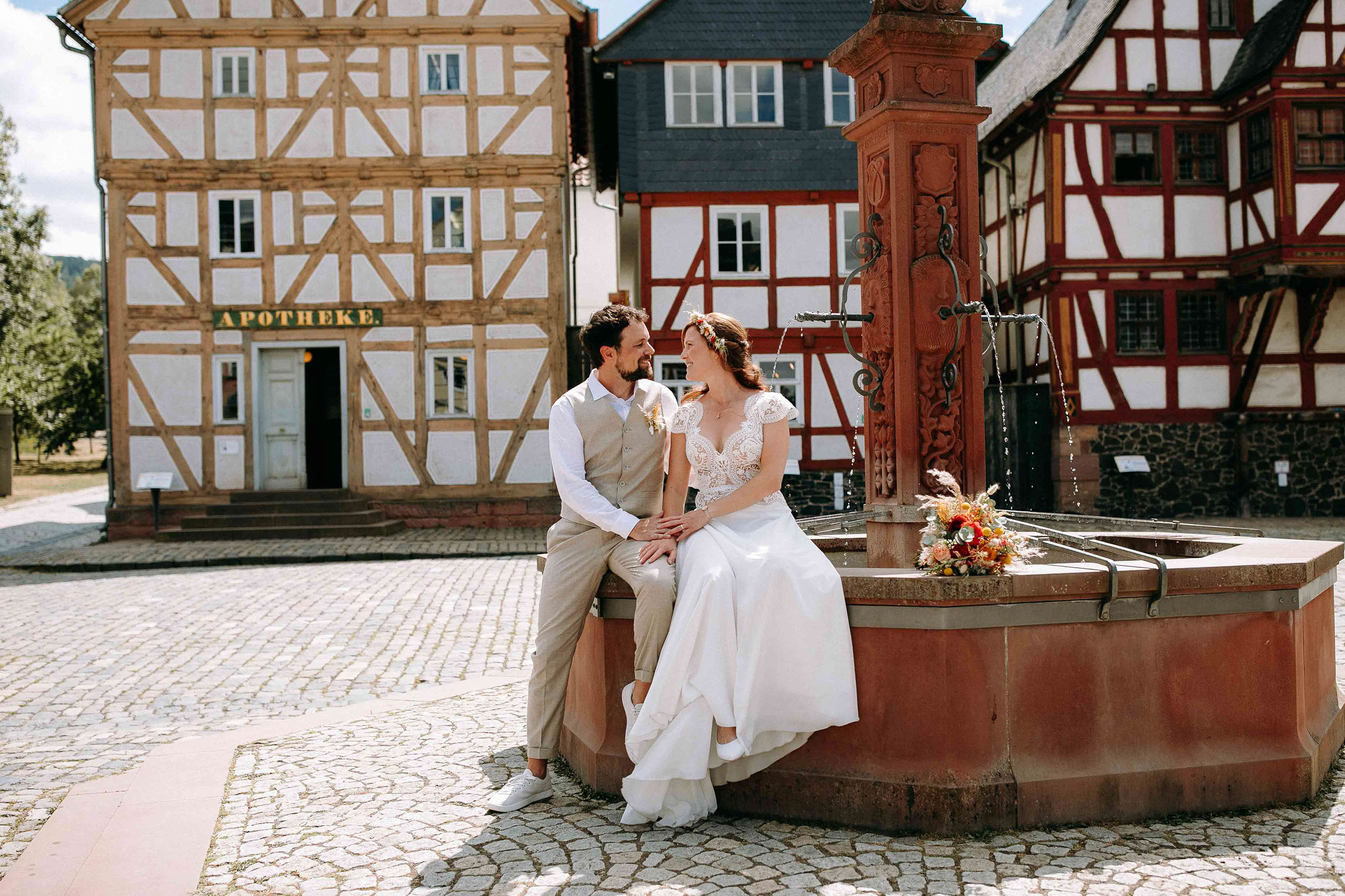 Romantisches Paarfoto am Brunnen vor Fachwerkhäusern im Freilichtmuseum Hessenpark – Hochzeitsfotograf Bad Homburg