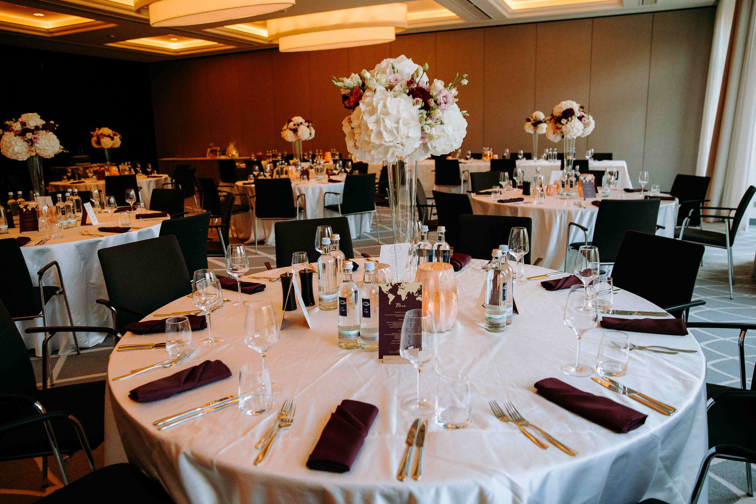 Runde Hochzeitstische mit weißer Tischdecke, lilafarbenen Servietten und Blumen im Dorint Hotel Oberursel.