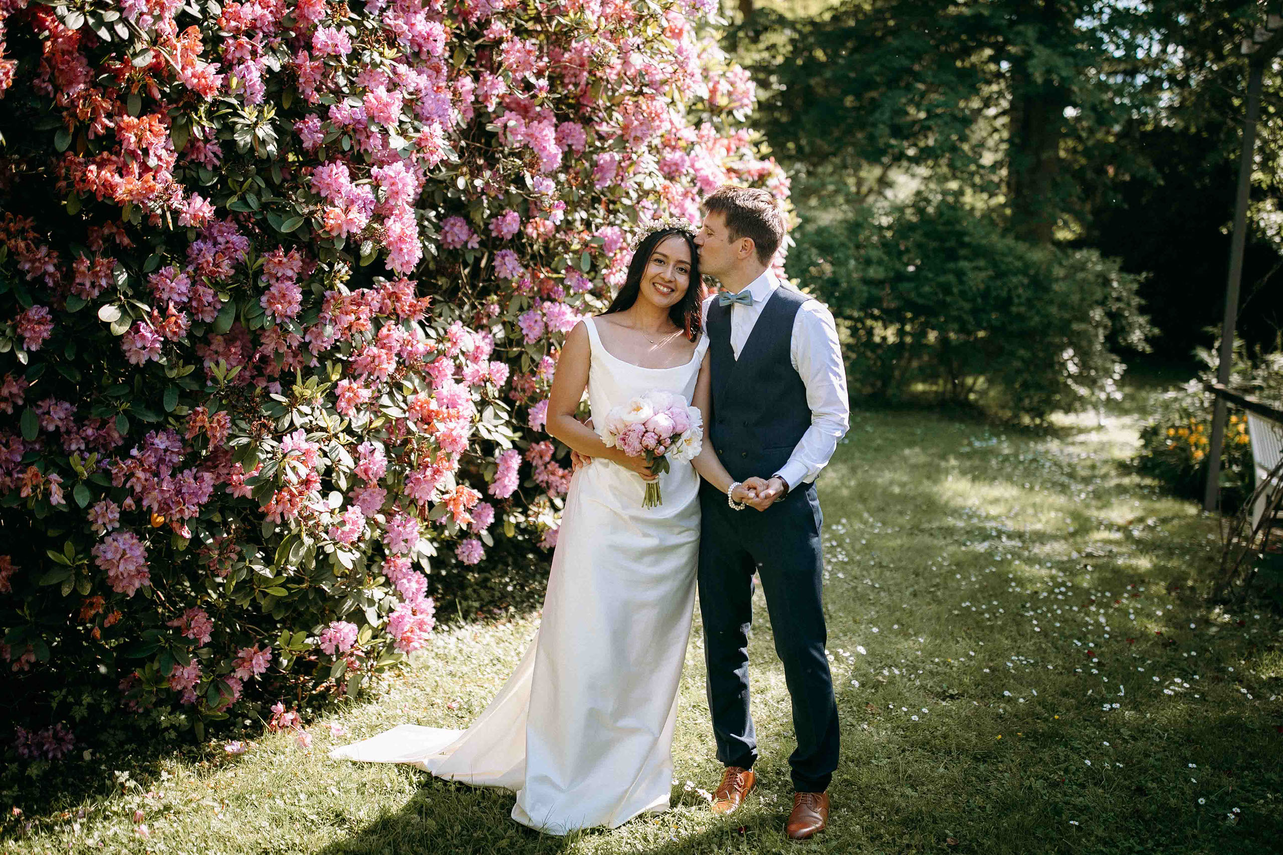 Brautpaar posiert vor farbenfrohem Rhododendron während der Hochzeitsfotos in Bad Homburg.