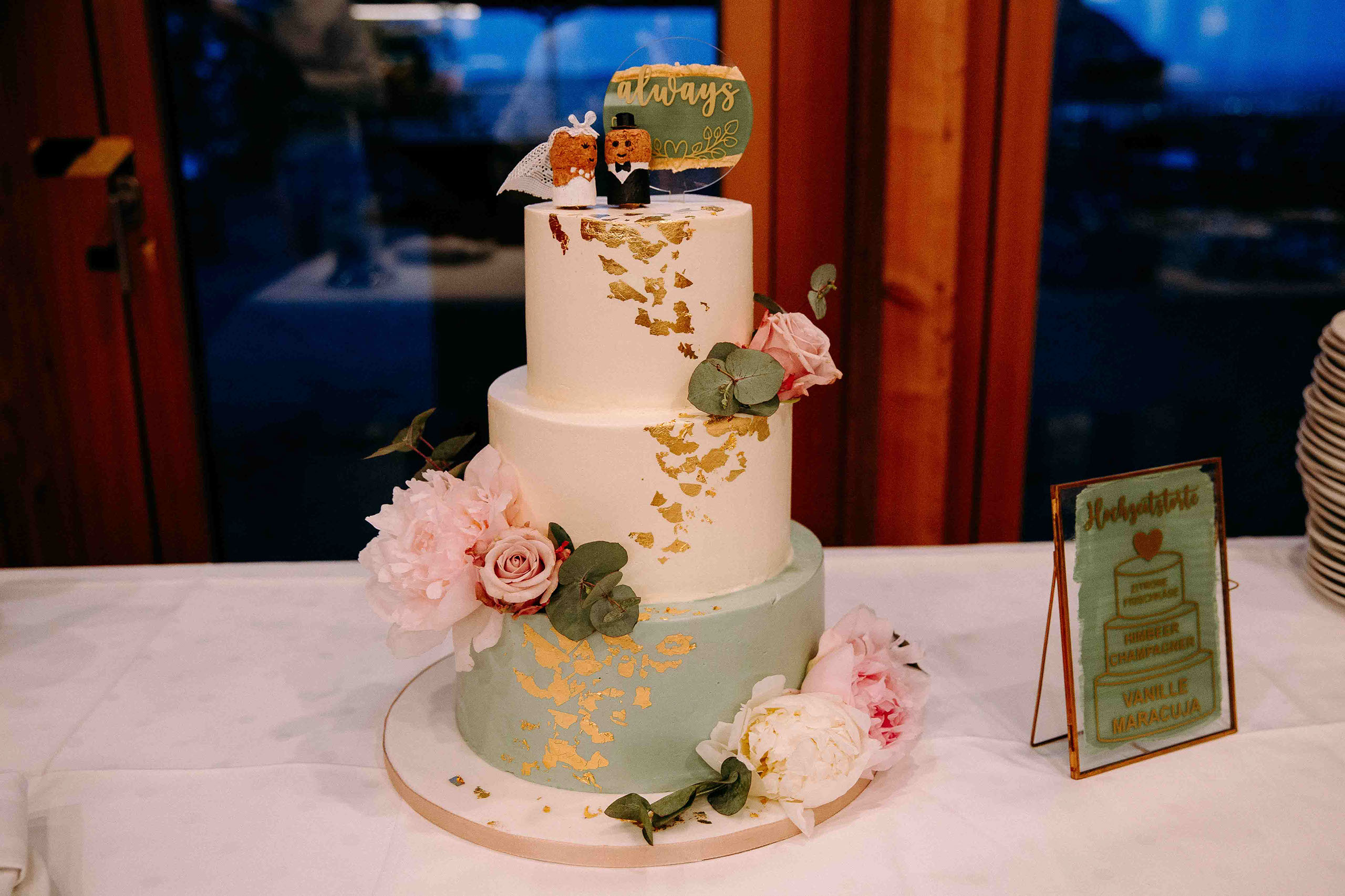 Weiße dreistöckige Hochzeitstorte mit goldenen Details und rosa Blumen in der Hochzeitslocation Am Niederwald im Rheingau.