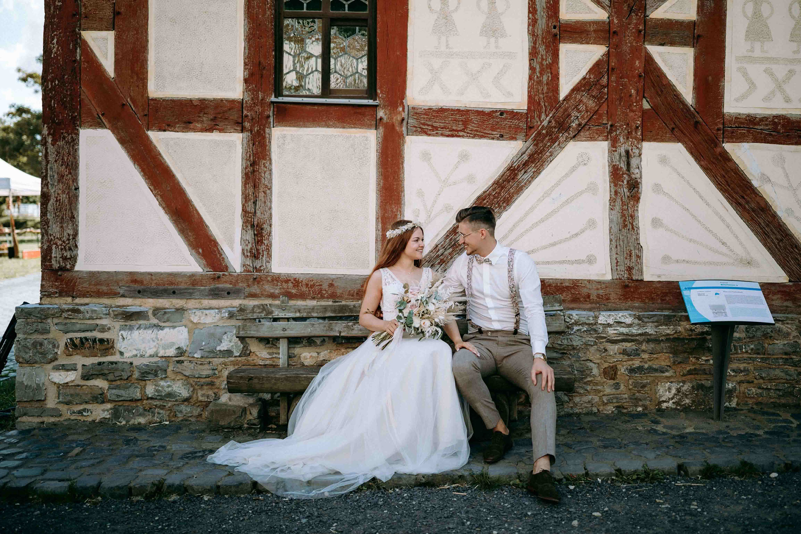 Brautpaar sitzt verliebt vor Fachwerkhaus im Freilichtmuseum Hessenpark – Hochzeitsfotos Bad Homburg.