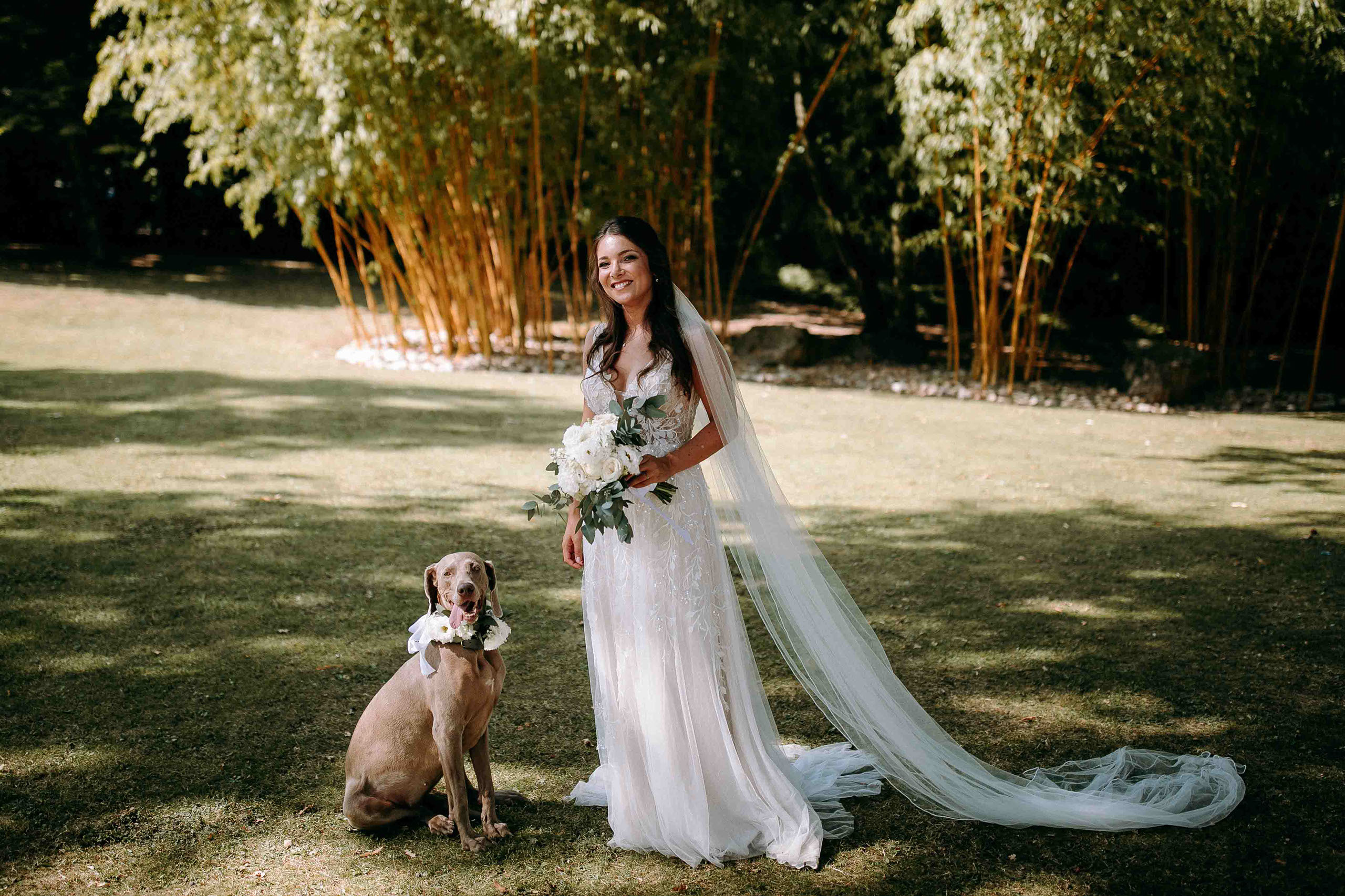 Braut mit Schleier und Blumenstrauß posiert im Garten der Burg Schwarzenstein mit Hund.