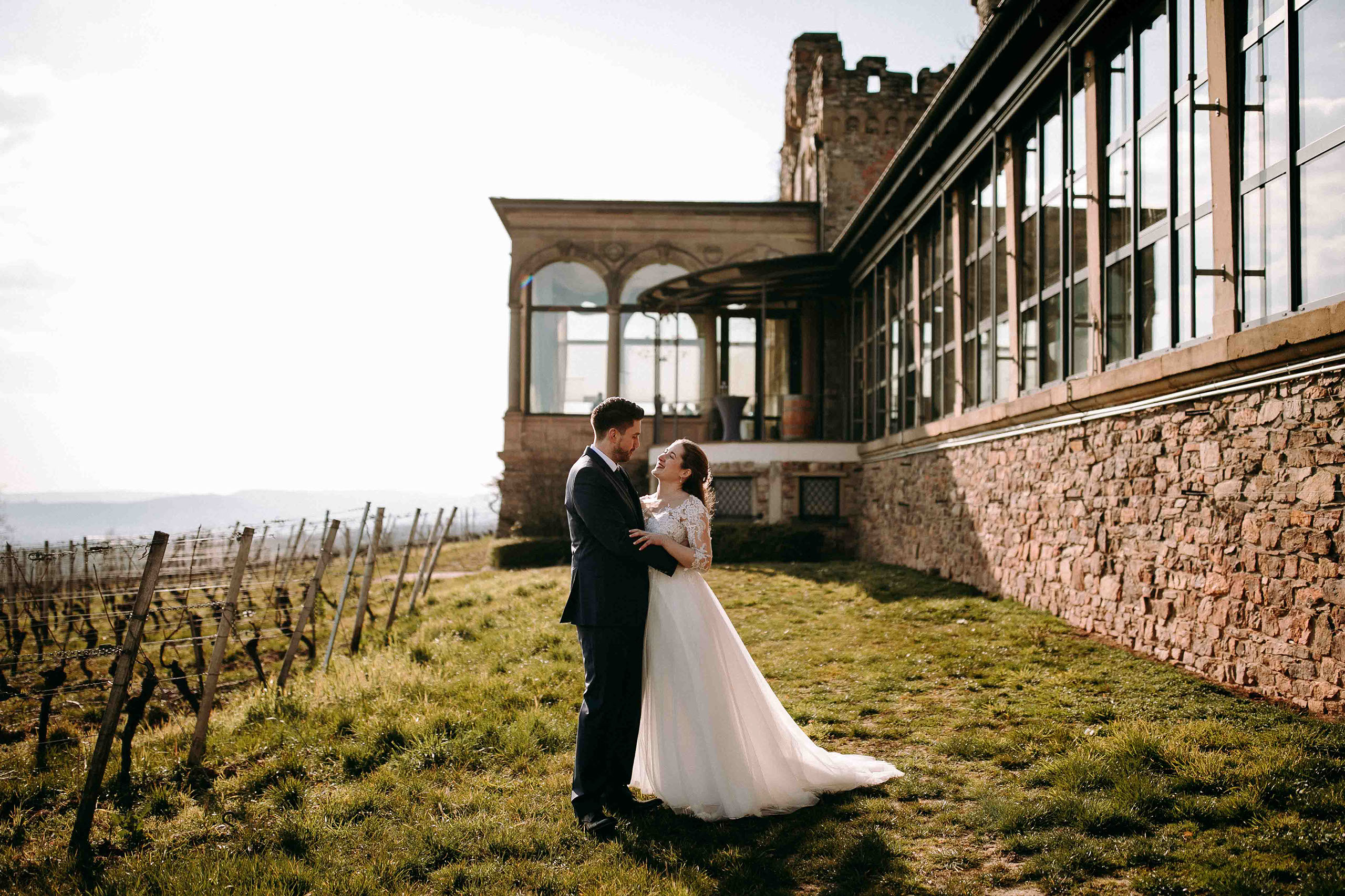 Romantisches Hochzeitsfoto des Brautpaars vor der Burg Schwarzenstein und Weinreben im Hintergrund.