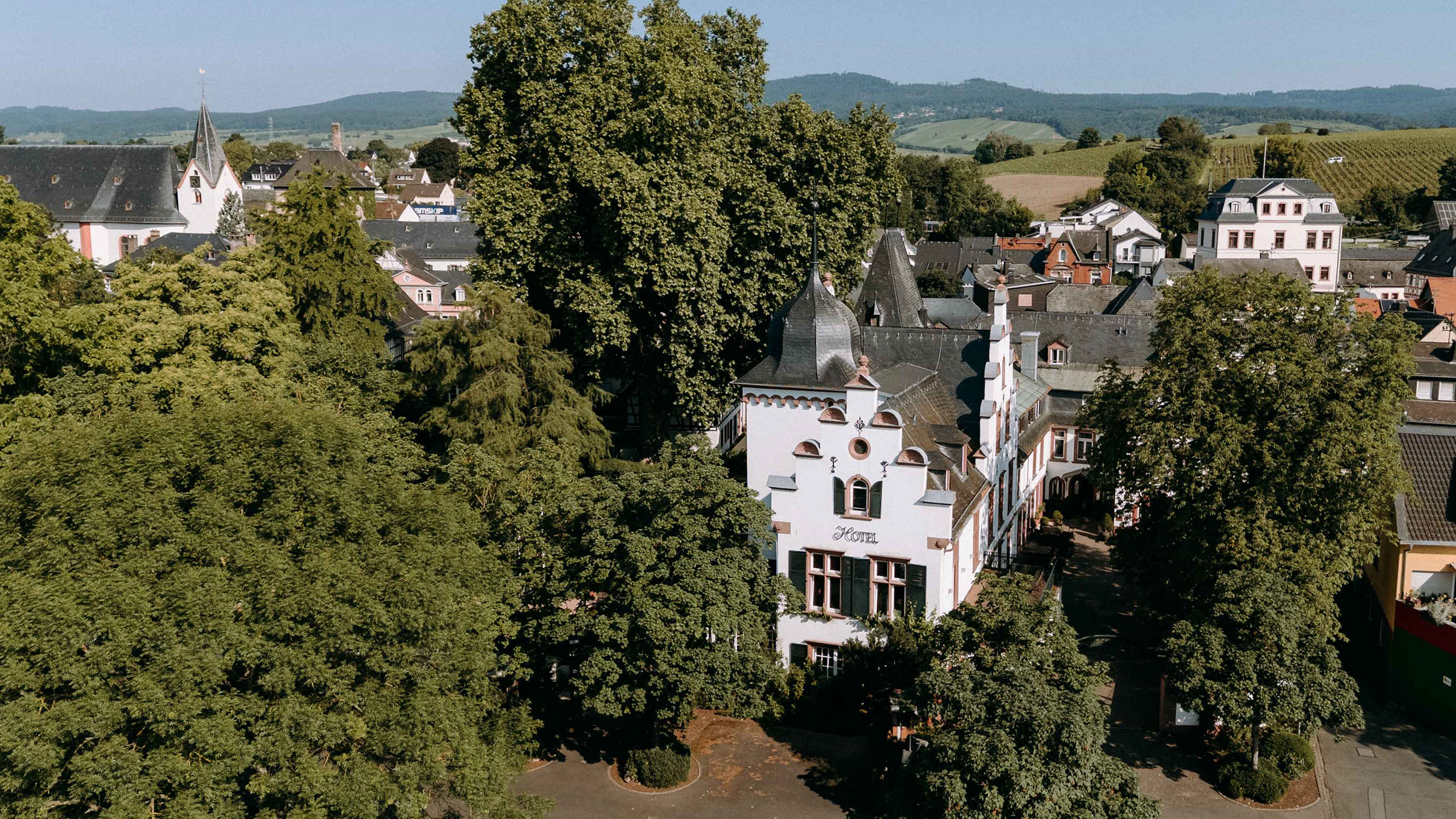 Außenansicht des historischen Hotel Kronenschlösschen in Eltville, umgeben von Bäumen und gepflegten Gartenanlagen – elegante Hochzeitslocation 