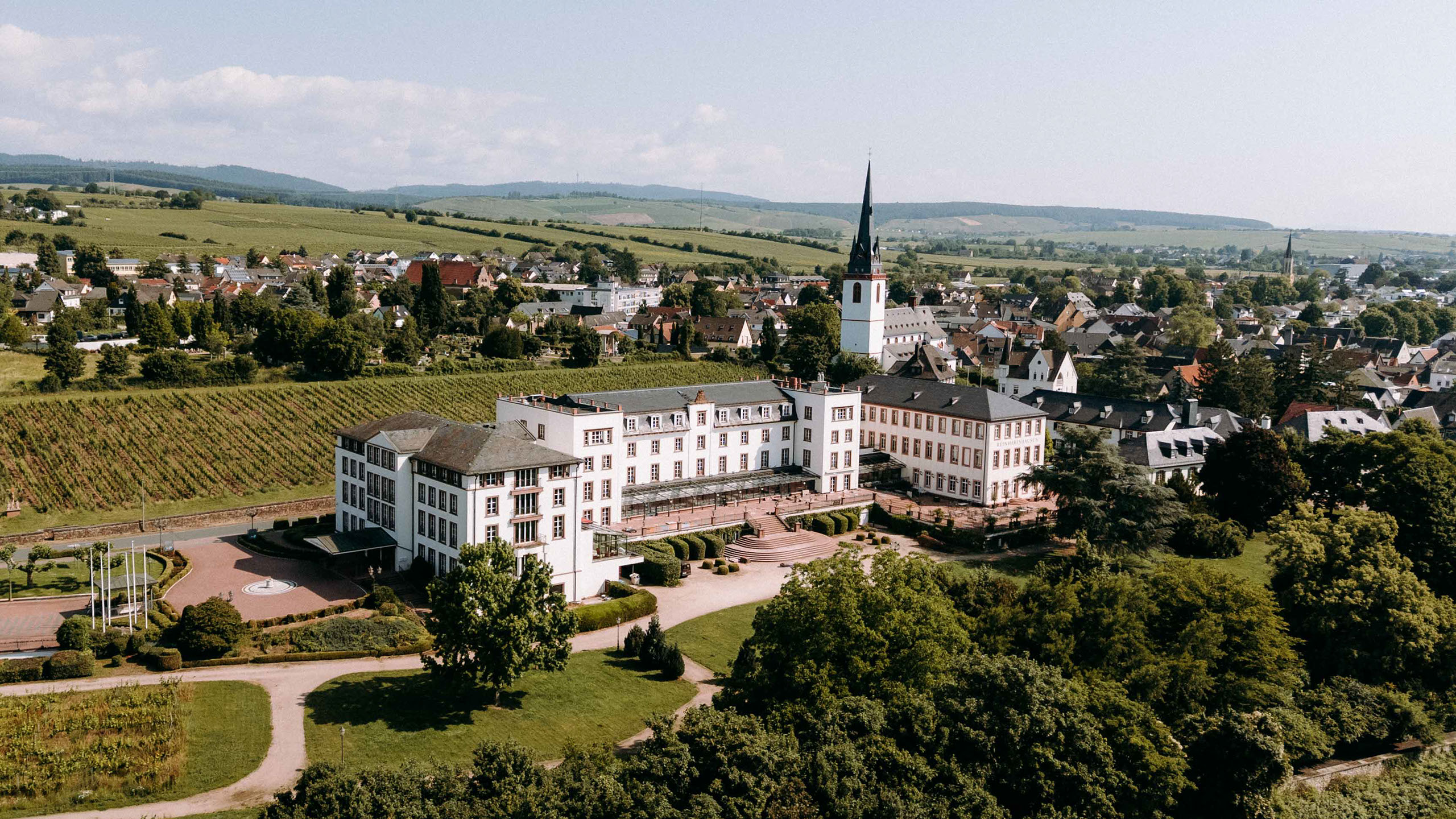 Luftaufnahme der symmetrischen Front von Schloss Reinhartshausen, eingerahmt von gepflegtem Schlossgarten, Weinreben –perfekte Hochzeitslocation