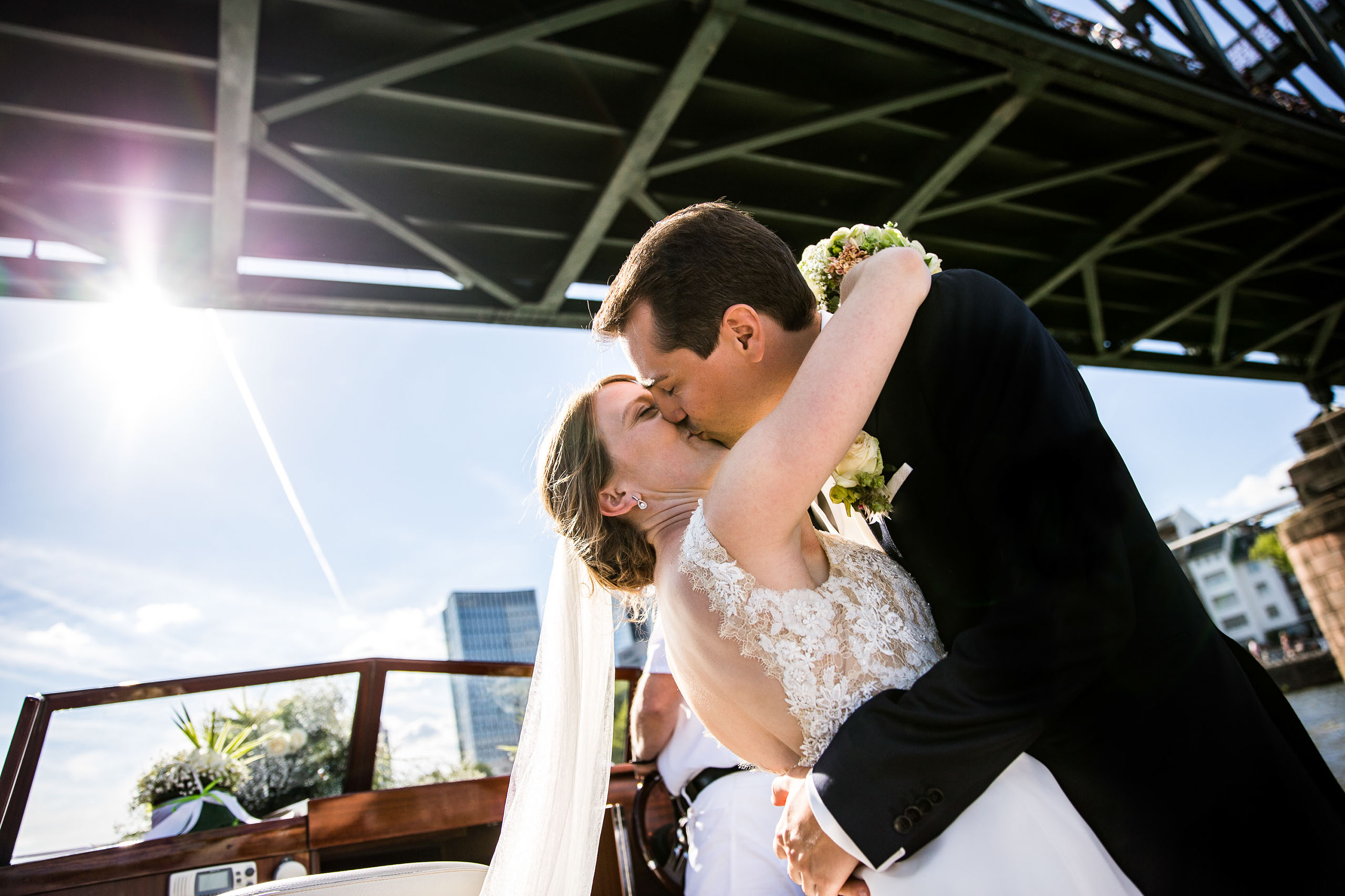 Das Brautpaar küsst sich auf einem Boot auf dem Main. Direkt unter dem Eisernen Steg in Frankfurt.